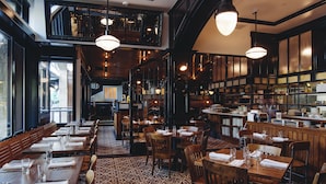 A restaurant with wooden tables and chairs, a patterned carpet, and hanging pendant lights.