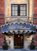The entrance of Hotel Ballard with a classic facade, a large sign above the entrance, and two potted plants on either side.