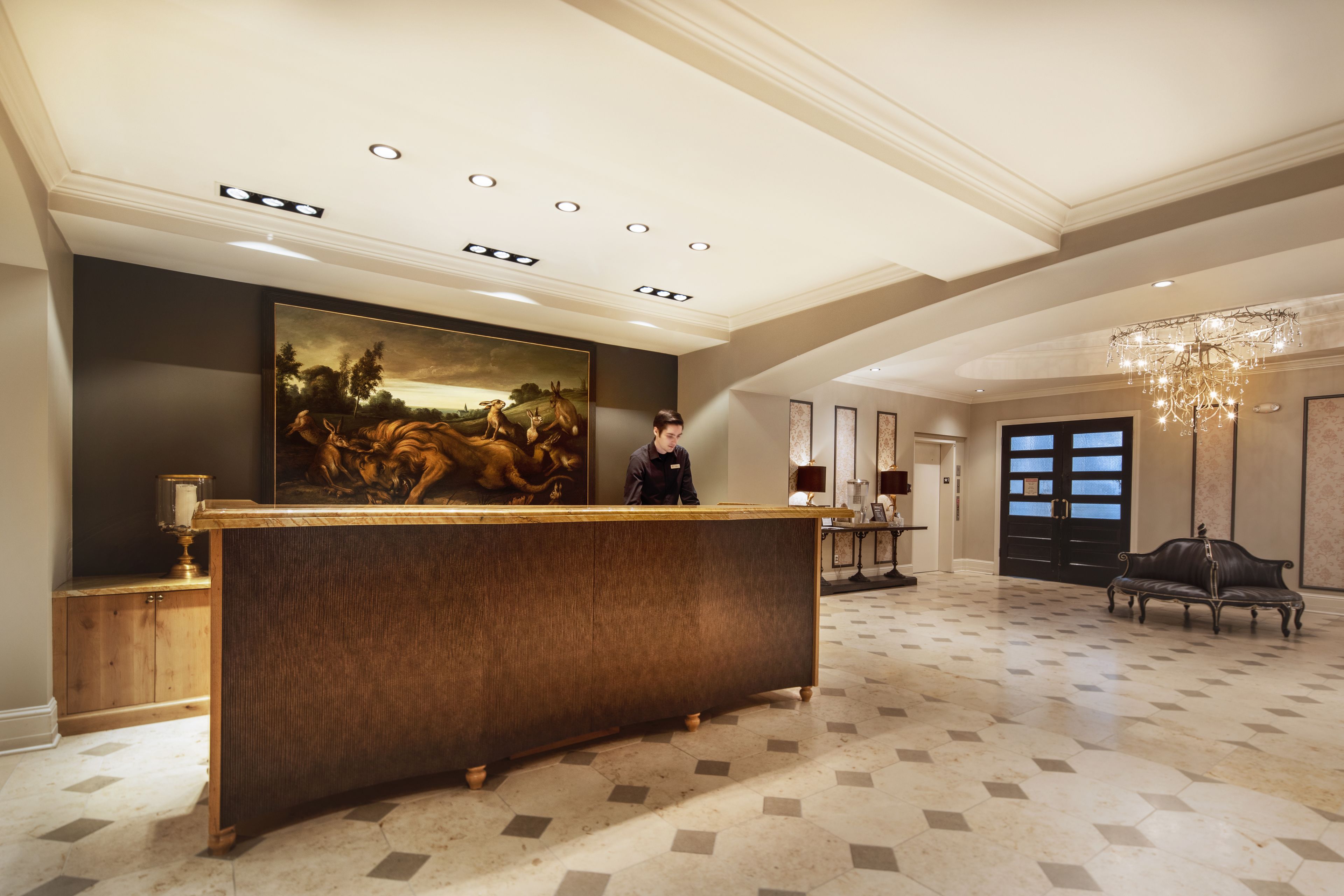 A reception area with a large painting, a wooden reception desk, a chandelier, and a black leather sofa.