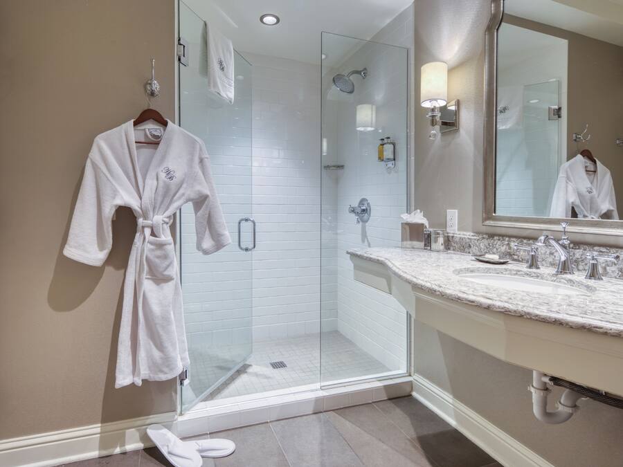 A modern bathroom with a glass-enclosed shower, a large mirror, and a marble countertop.