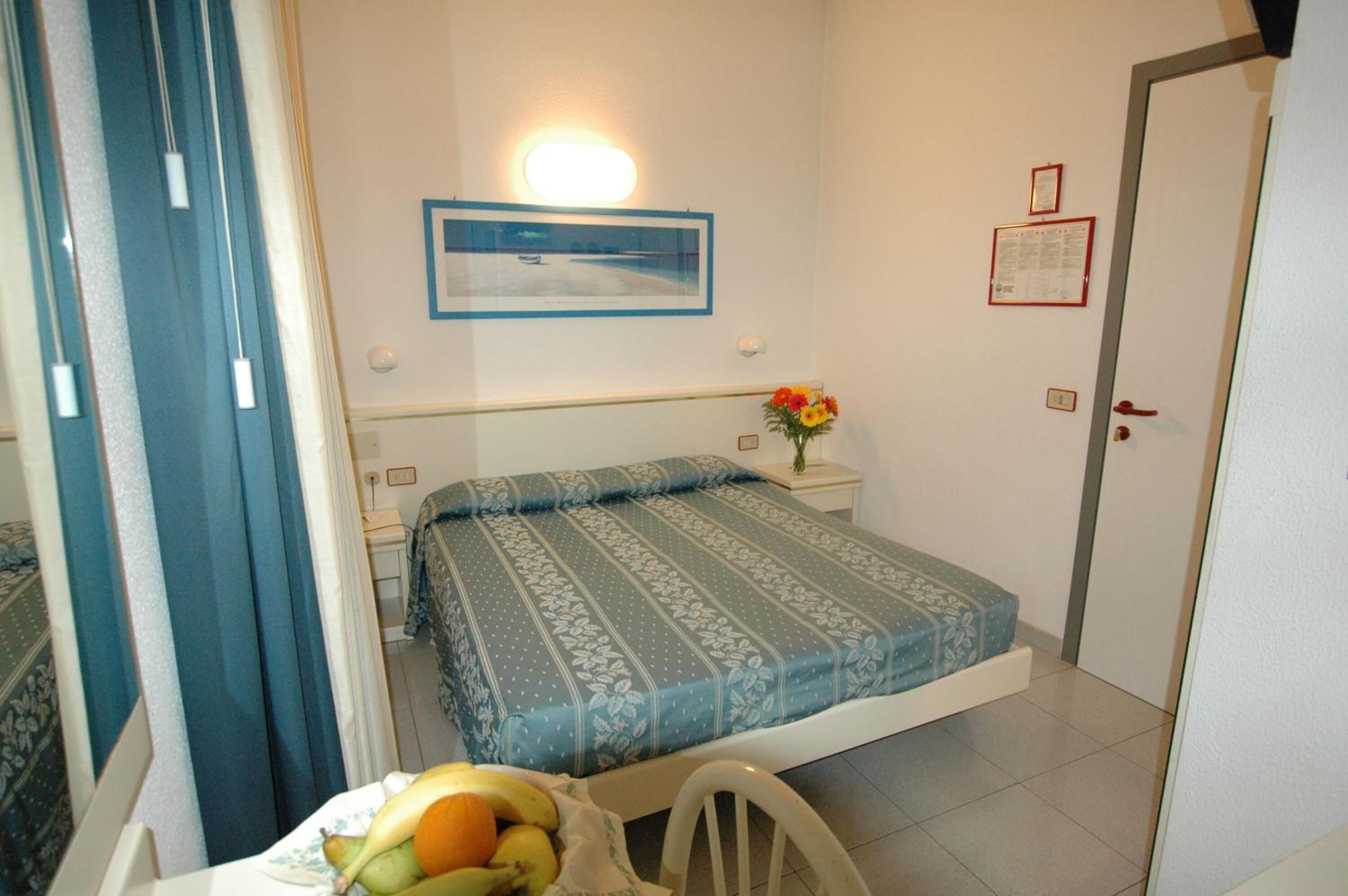 A bedroom with a bed, a nightstand, a framed picture on the wall, and a door.