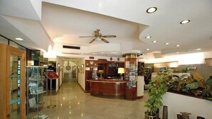 A hotel lobby with a reception desk, a ceiling fan, and a glass display case with items. - Hotel Crystal & Residence (Portoferraio)