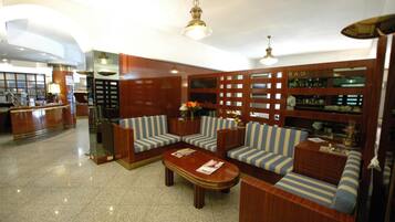 A lobby with a reception desk, striped sofas, a wooden coffee table, and a bar area with a sign reading "BAR".