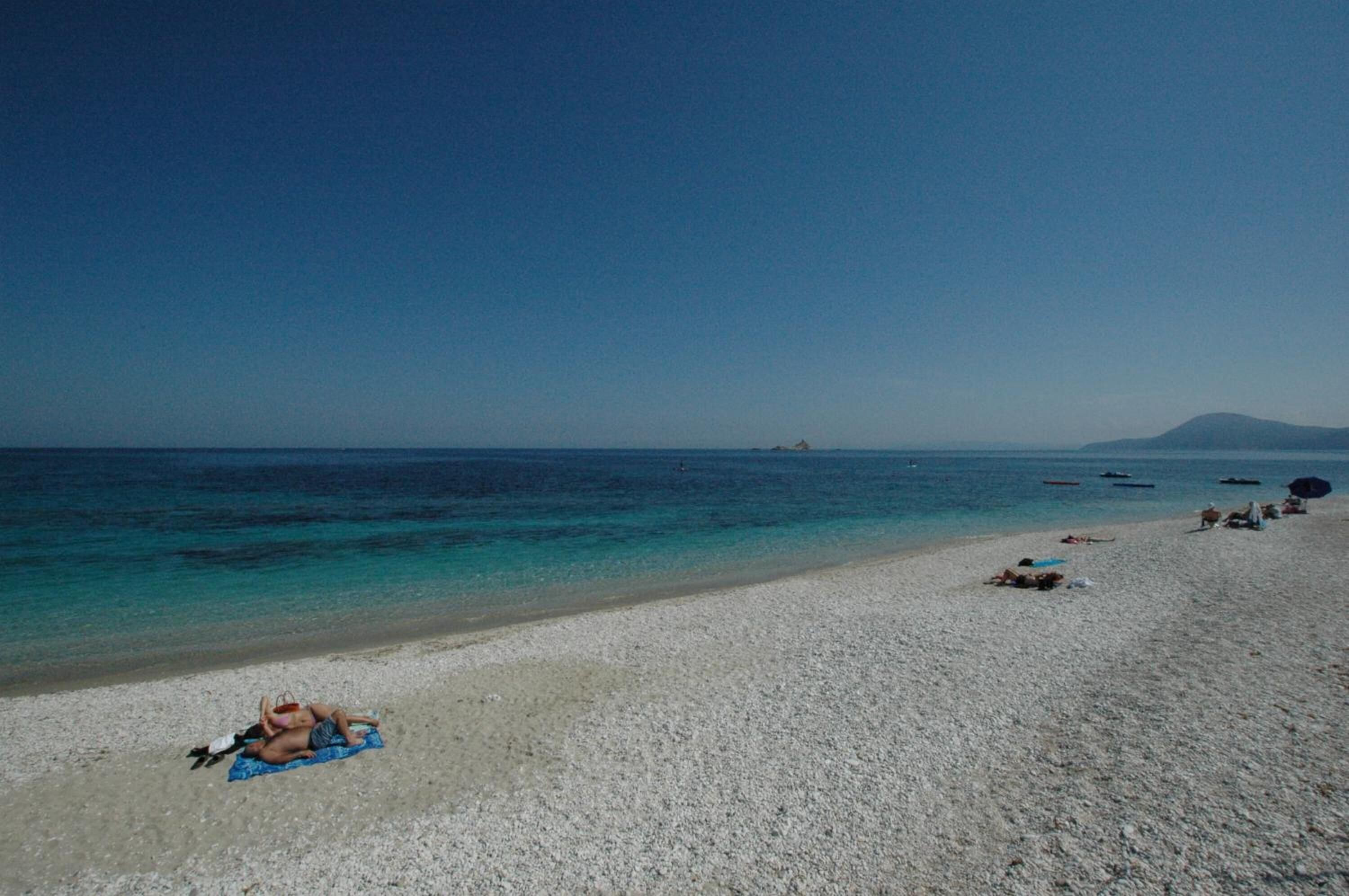 A beach with a clear sky, calm sea, and a distant mountain.
