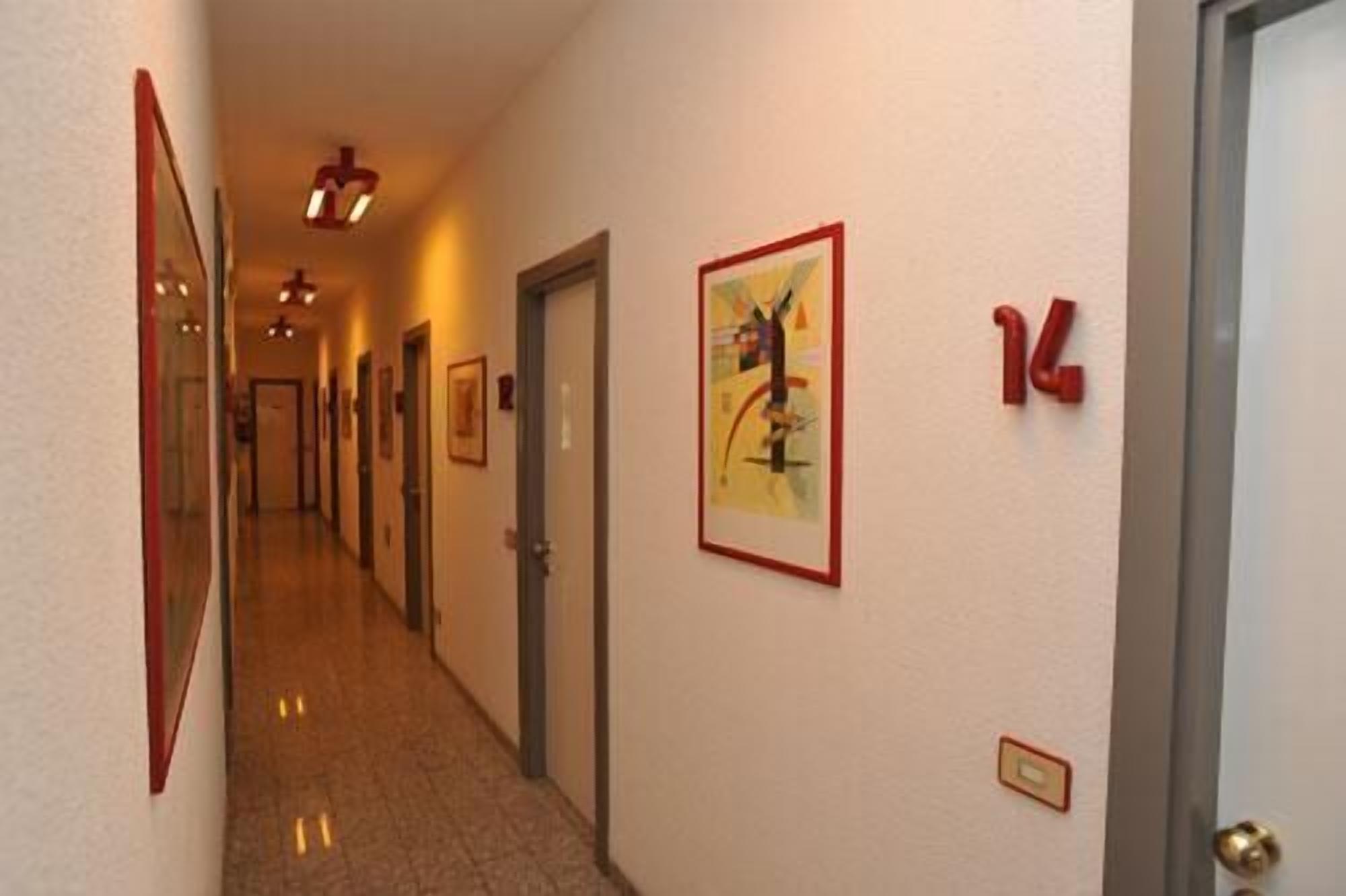 A hotel hallway with doors, numbered signs, and framed artwork on the walls.
