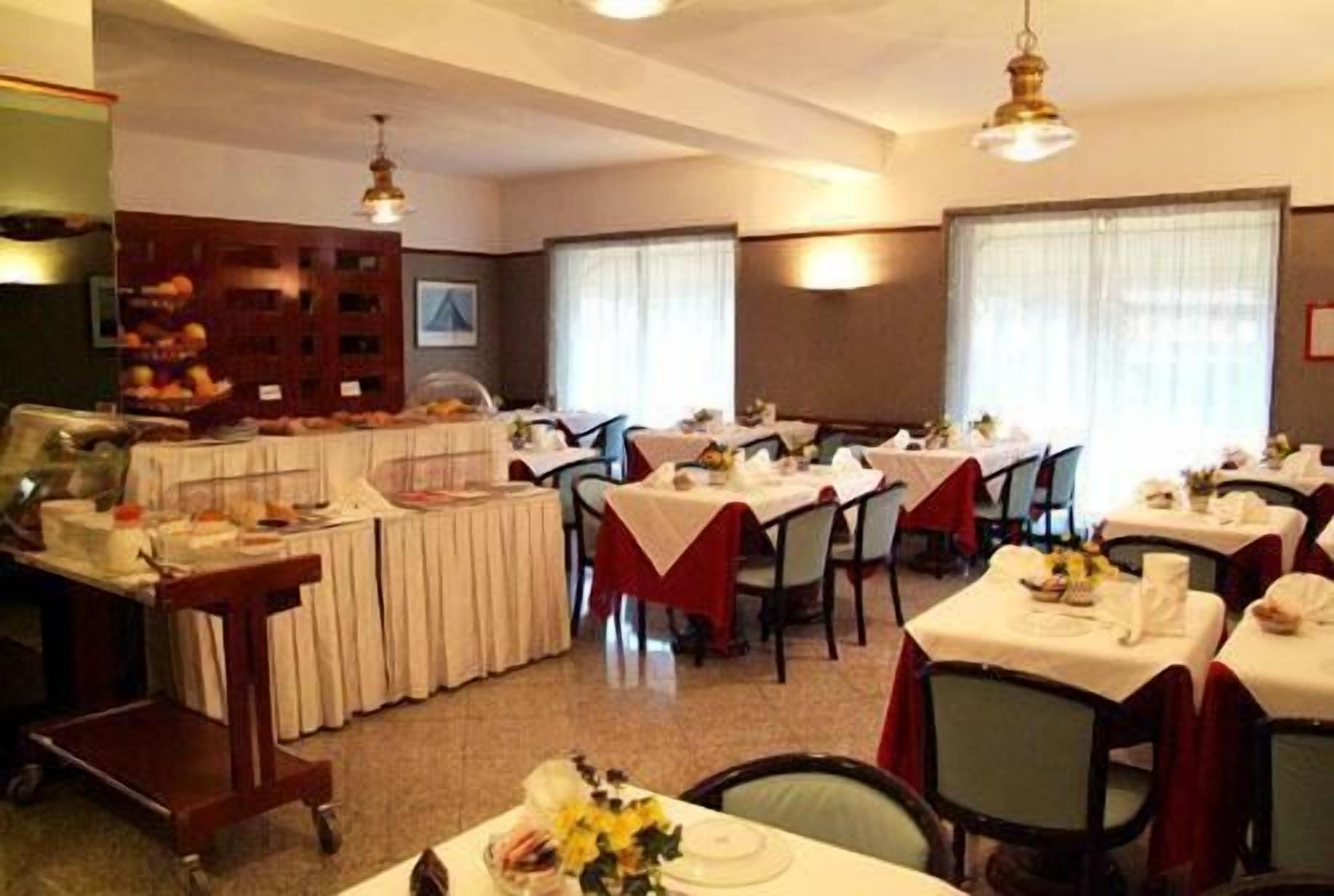 A dining area with multiple tables set for meals, a buffet area with food items, and a kitchen in the background.