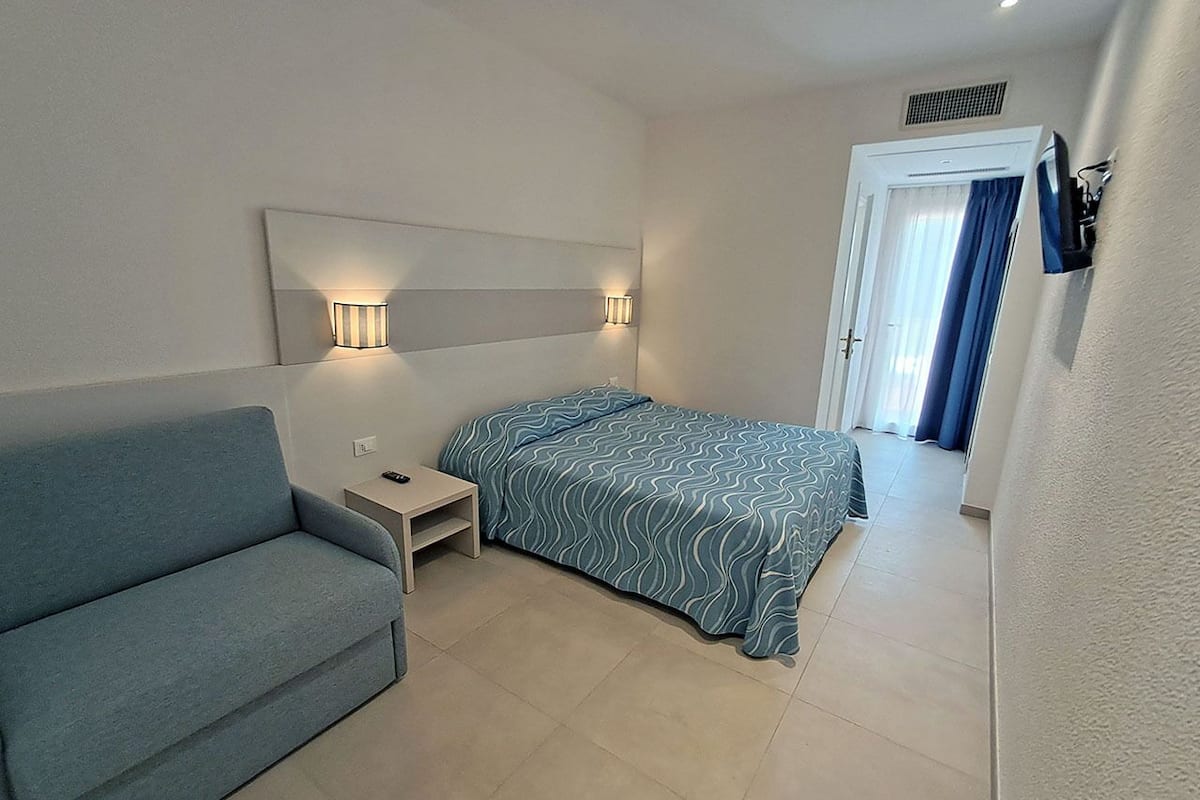A bedroom with a bed, a sofa, a nightstand, and a wall-mounted TV.