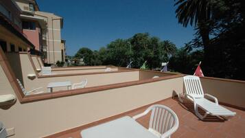 A rooftop terrace with white lounge chairs, a table, and a small pool area.