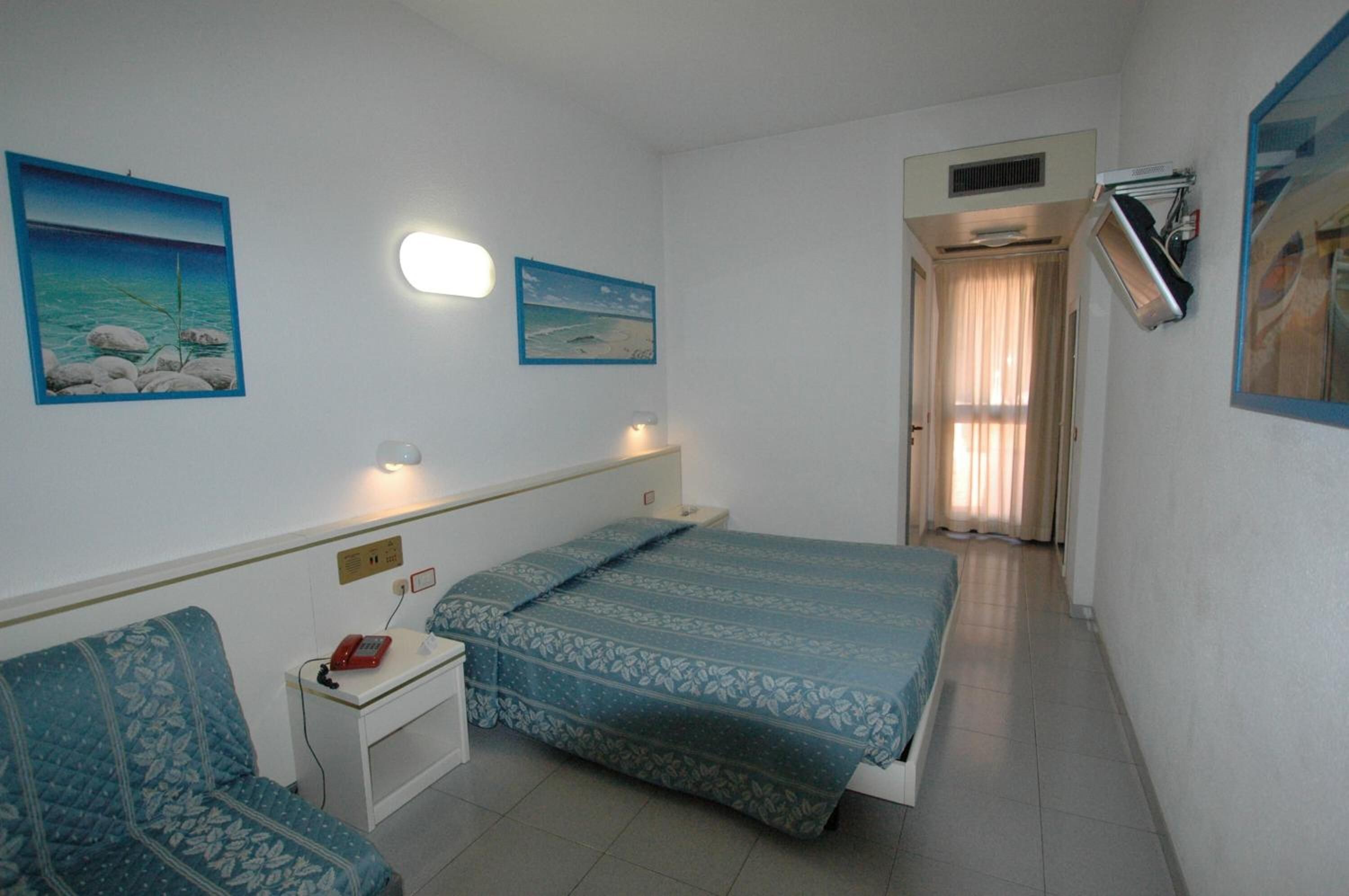 A bedroom with a bed, bedside table, and a chair. There are two wall-mounted lights and a ceiling fan.