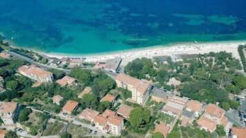 Vista aérea de uma cidade costeira com edifícios, uma praia e águas azuis cristalinas.
