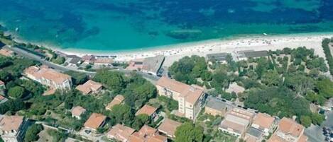 An aerial view of a coastal town with buildings, a beach, and clear blue waters.