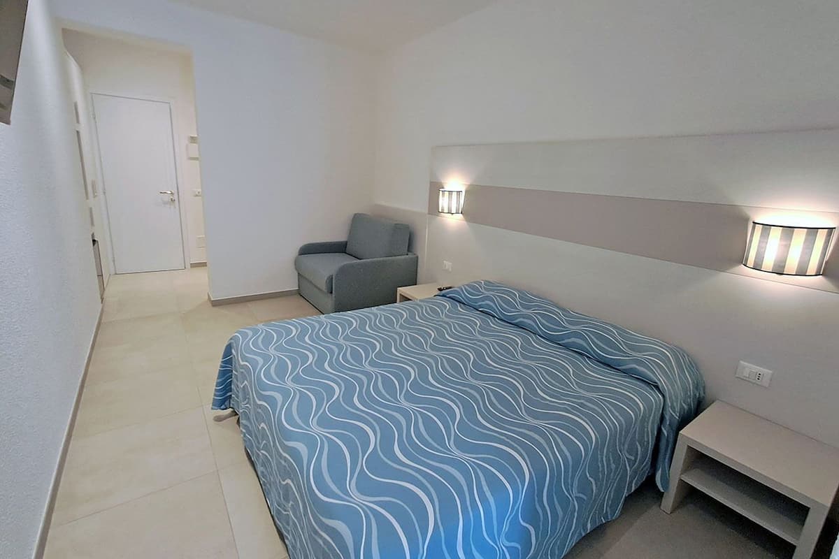 A bedroom with a bed, a chair, and two wall-mounted lights.