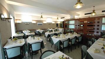 Une salle à manger avec plusieurs tables dressées pour le service, chacune étant recouverte d’une nappe blanche et entourée de chaises vertes.
