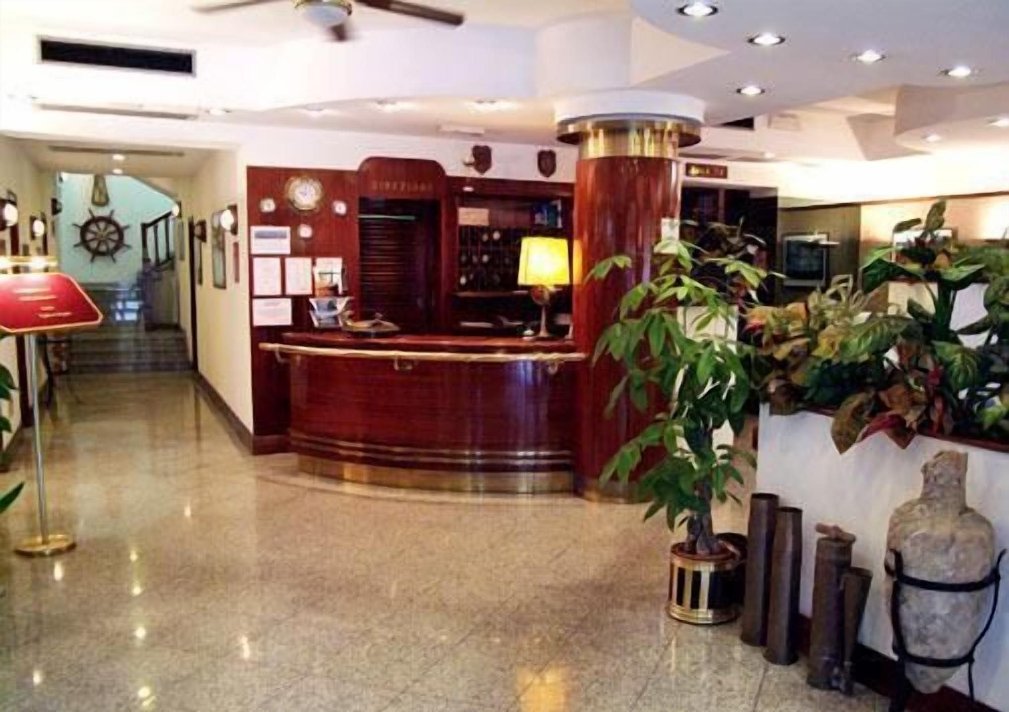 A hotel reception area with a wooden reception desk, a large potted plant, and a stone sculpture.