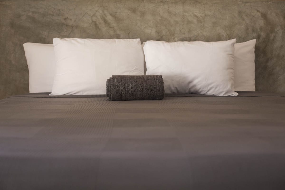 Una cama con un colchón gris, cuatro almohadas blancas y una manta gris.