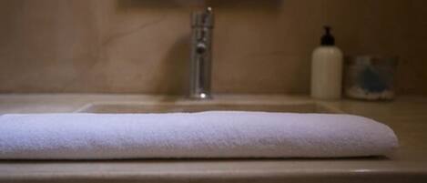 Un bagno con un asciugamano bianco sul lavandino, un rubinetto e una saponetta.