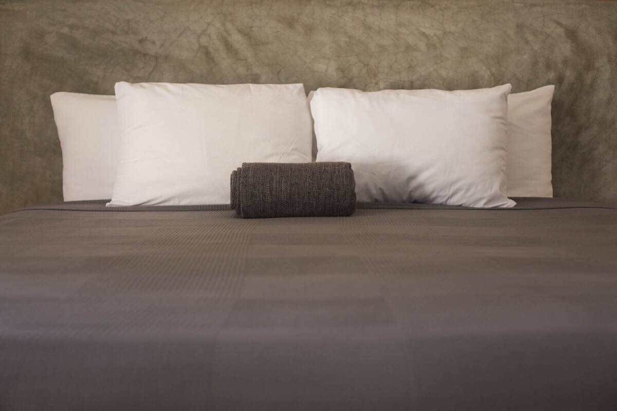 Una cama con una colcha gris y cuatro almohadas blancas.