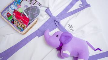 A crib with a purple elephant toy, a basket with baby products, and a white blanket with purple stripes.