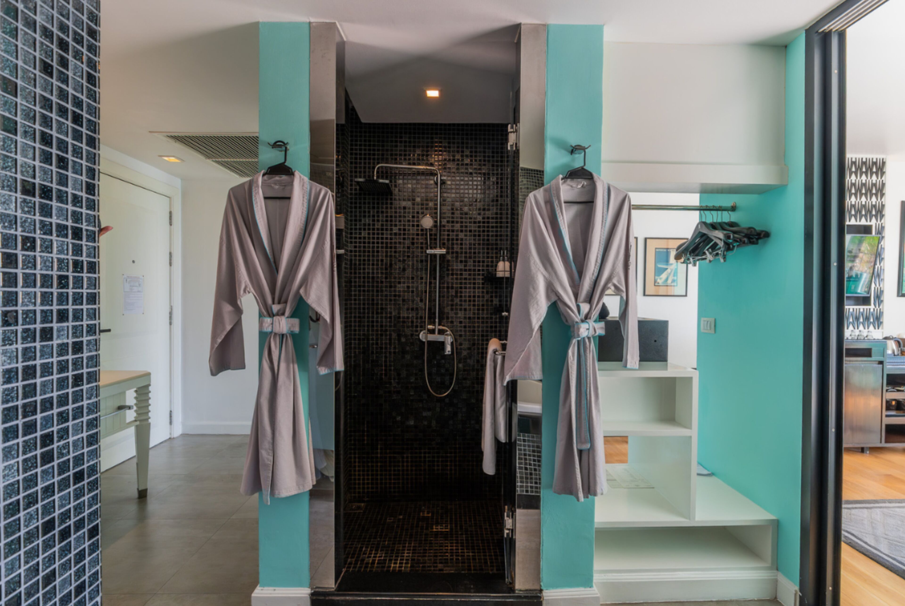 A modern bathroom with a glass shower enclosure, two robes hanging on hooks, and a teal accent wall.