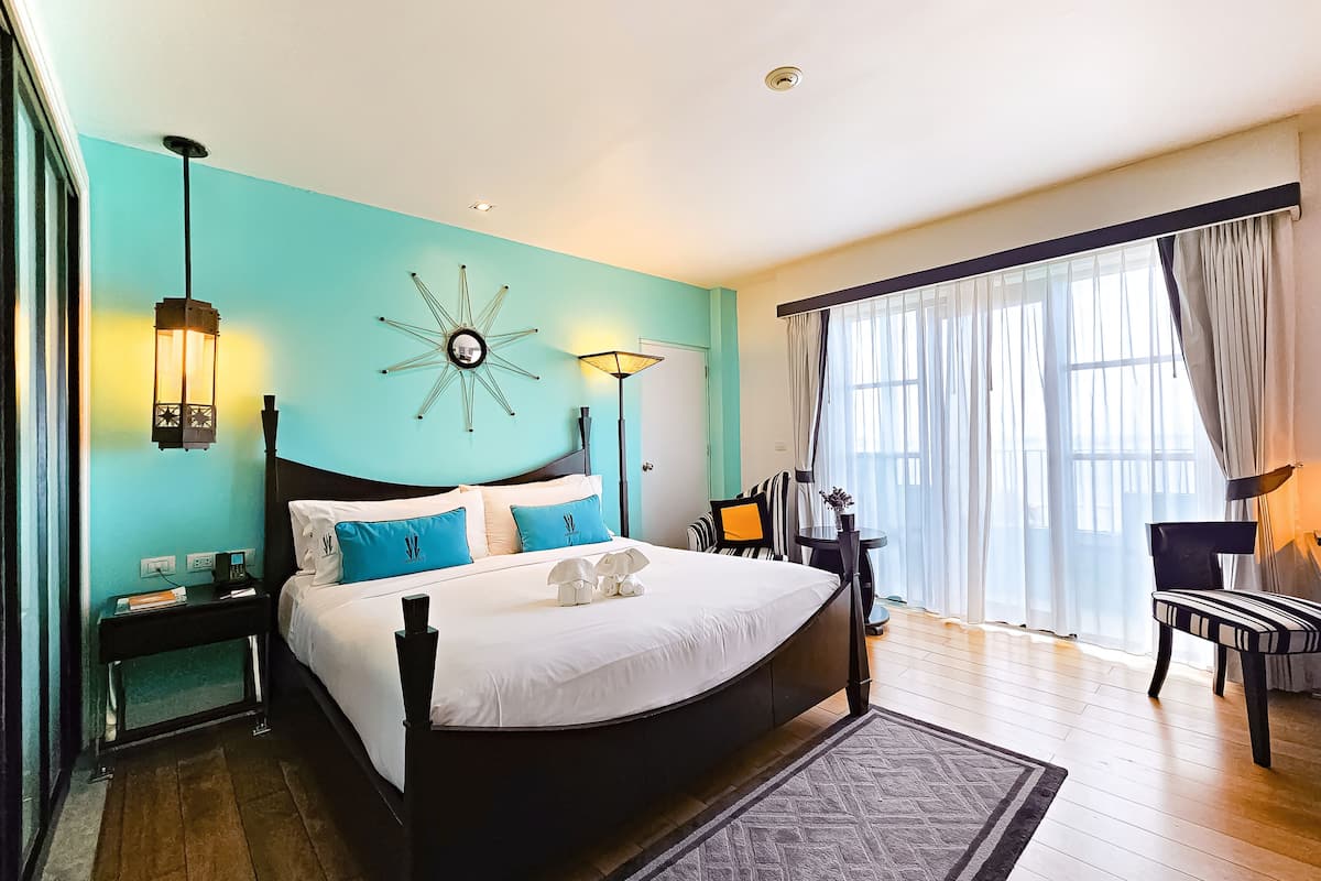 A modern hotel room with a large bed, a desk, a chair, and a large window with curtains.