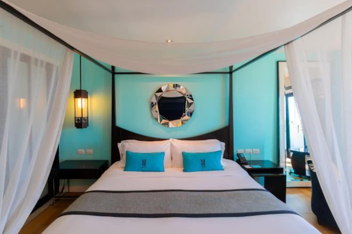 A bedroom with a bed, two bedside tables, a mirror, and a hanging light fixture.