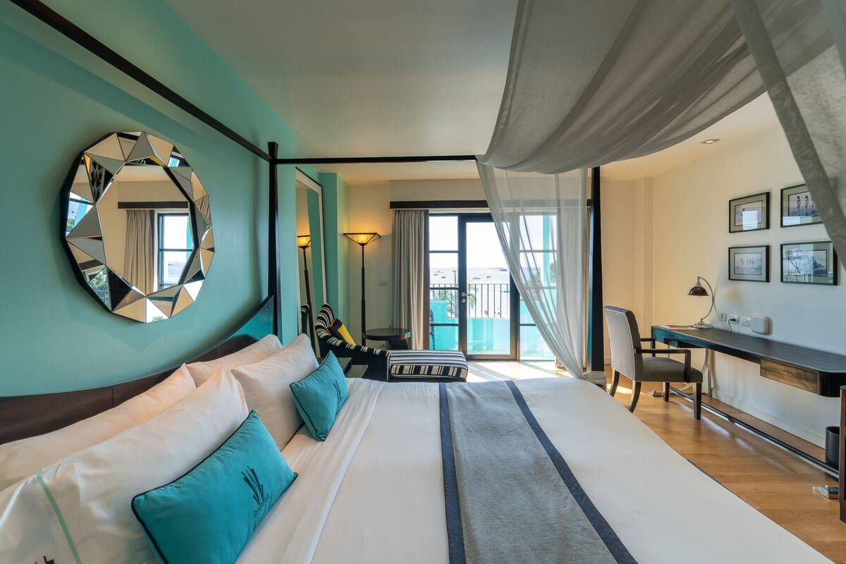 A hotel room with a large bed, a desk, a chair, a mirror, and a view of the outdoors.