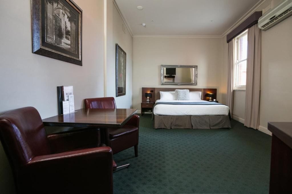 A hotel room with a bed, a desk, a chair, a dresser, and a large mirror.