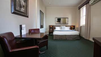 A hotel room with a bed, a desk, a chair, a dresser, and a large mirror.