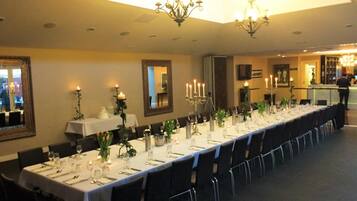 A long dining table set with white tablecloths, candles, and glassware, in a room with chandeliers and framed artwork on the walls.