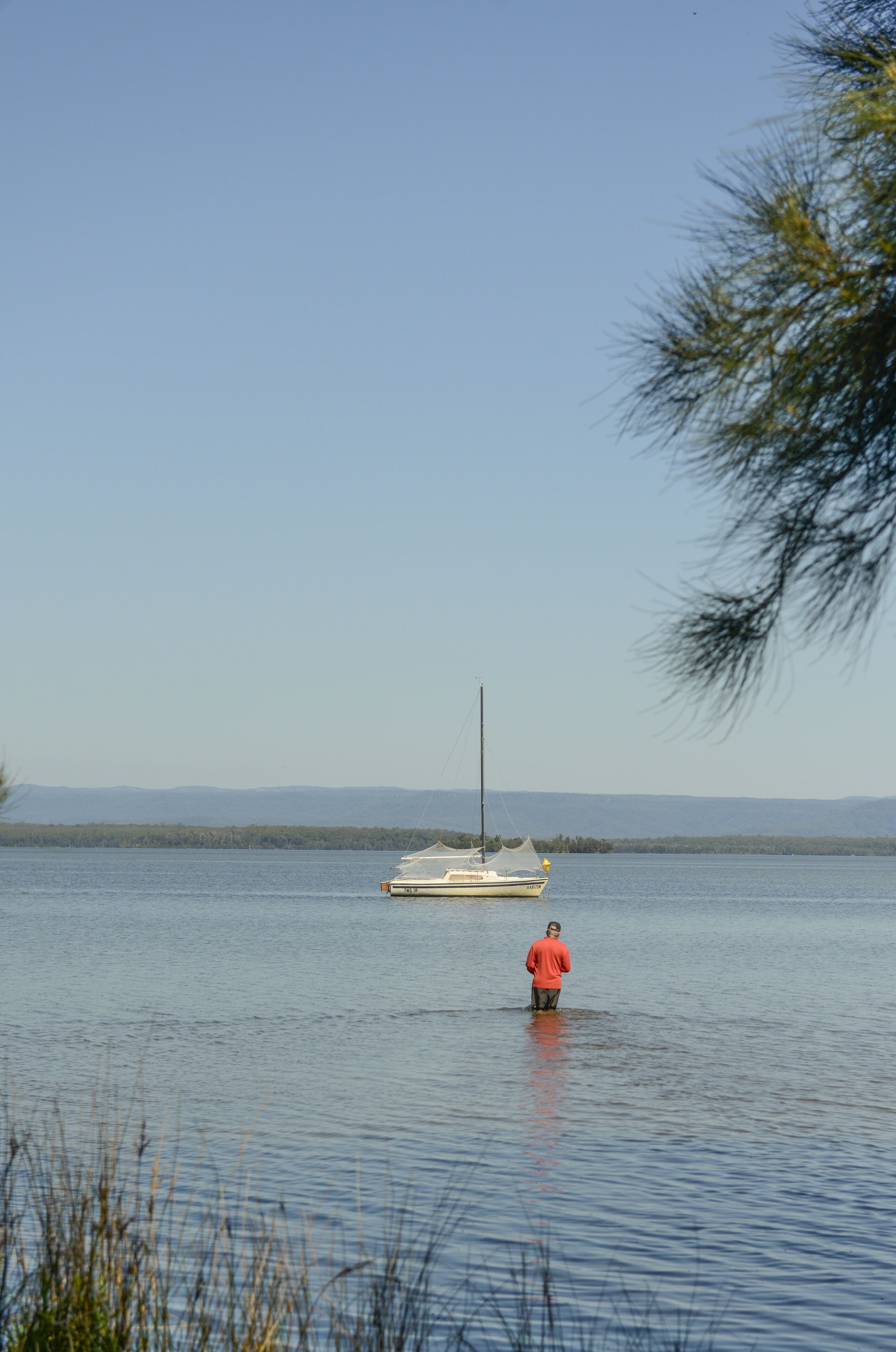 A calm lake with a boat and a person standing in the water.