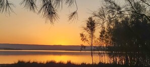 Un atardecer sobre un lago tranquilo, con siluetas de árboles y colinas a lo lejos.