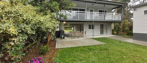 A two-story house with a balcony, a patio with chairs, and a well-maintained lawn.