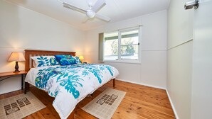 Et soveværelse med en træseng, ventilator i loftet, et vindue og to sengeborde med lamper.