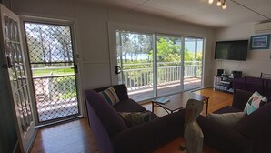 En stue med sofa, sofabord og fjernsyn. Der er en balkon med gelænder og en dør med myggenet.