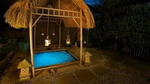 A thatched-roof structure with a pool, surrounded by stone tiles and potted plants. - Plantation House (Rye)
