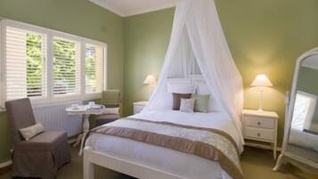 A bedroom with a canopy bed, a chair, a small table, and a nightstand with lamps.