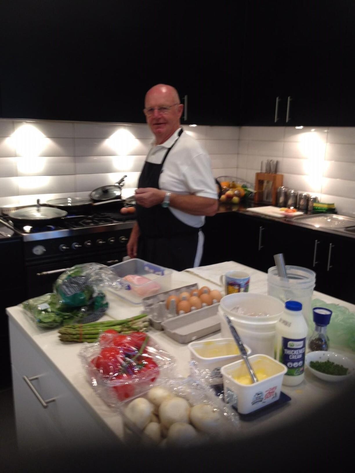 A kitchen with a chef standing by a counter filled with ingredients and cooking utensils.