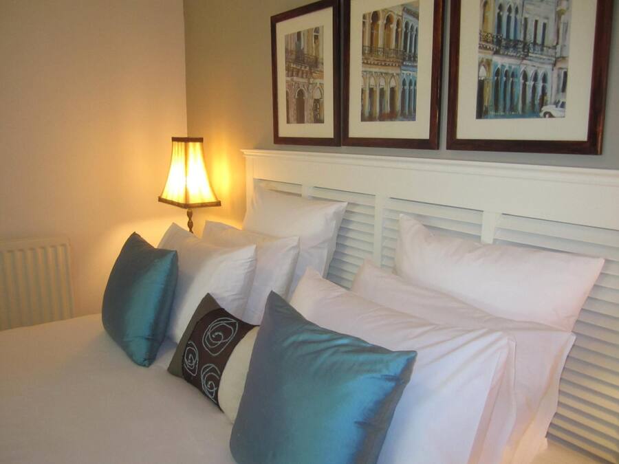 A neatly made bed with white and blue pillows, a bedside lamp, and framed pictures on the wall.