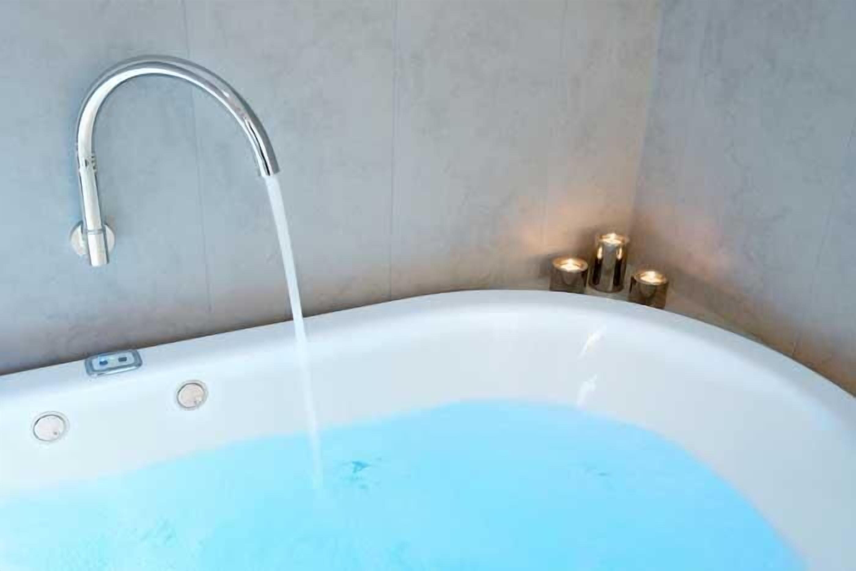 A bathtub with running water, a modern faucet, and a light fixture on the wall.