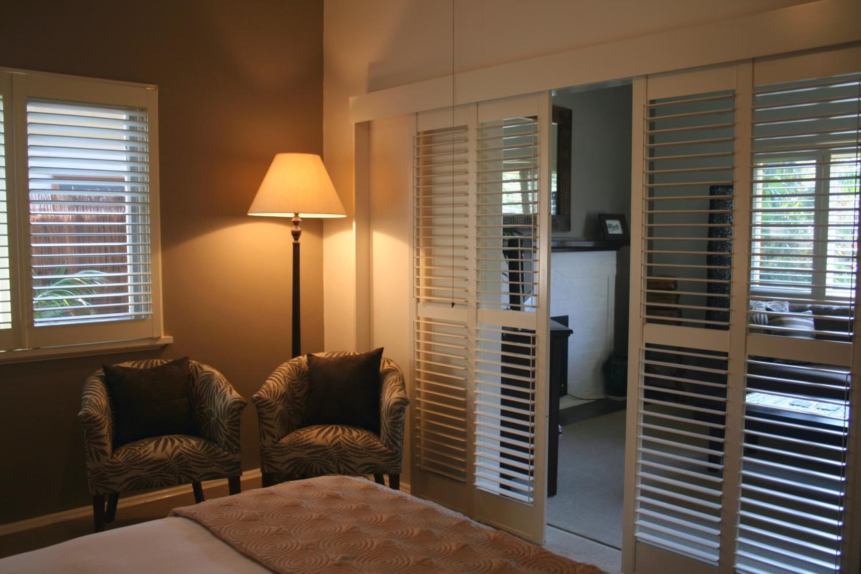 A bedroom with a bed, two chairs, a lamp, and a sliding door leading to a bathroom.