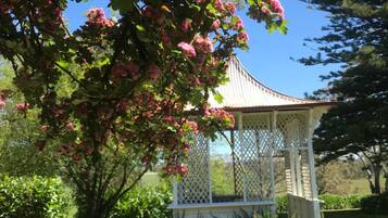 A gazebo with a lattice roof, surrounded by lush greenery and a clear blue sky.