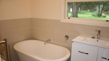 Une salle de bain avec une baignoire, un lavabo et une fenêtre donnant sur les arbres.