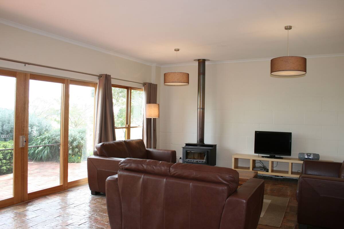 A spacious living room with leather sofas, a fireplace, a television, and a large sliding glass door leading to a patio.