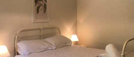 A neatly made bed with white linens, a bedside lamp, and a bedside table.