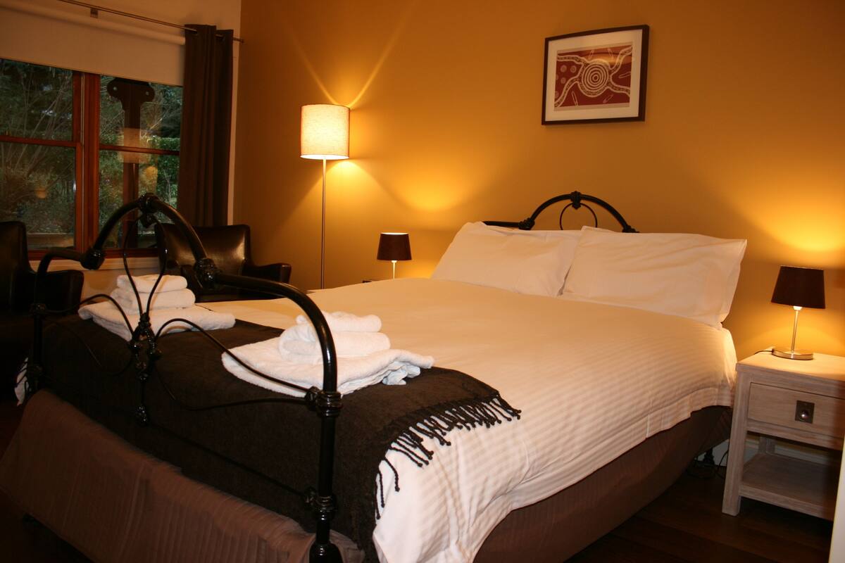A neatly made bed with white linens, a bedside table with a lamp, and a window with curtains.