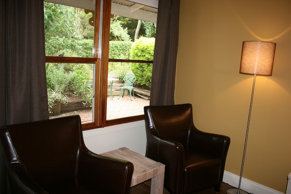 A room with two leather chairs, a small wooden table, a floor lamp, and a window with a view of greenery outside.