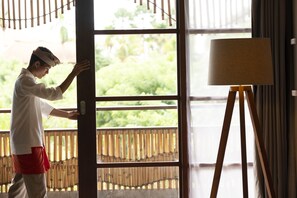 A person standing by a window with a view of greenery outside.
