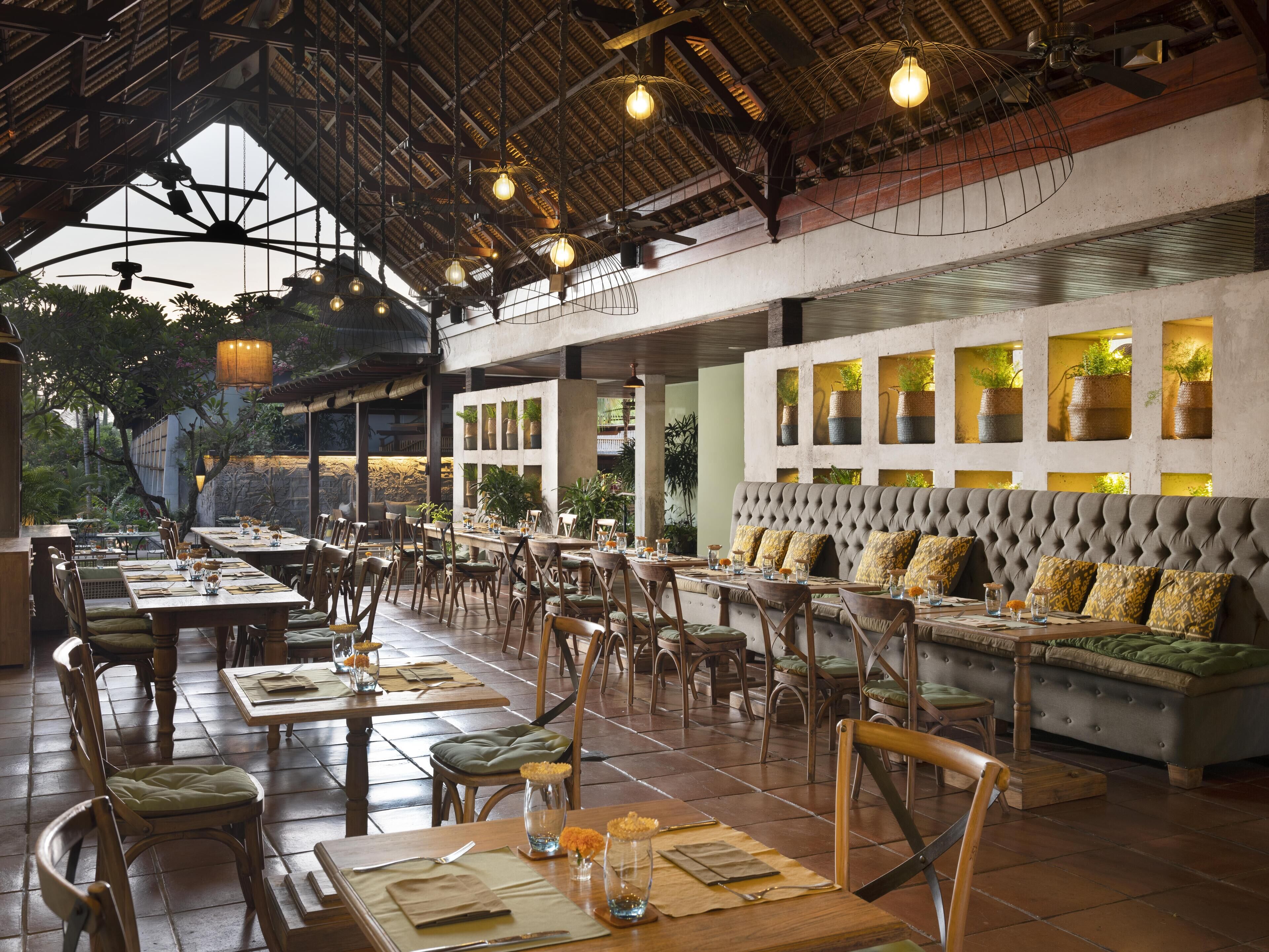 Un restaurante con mesas y sillas de madera, un banco acolchado y lámparas colgantes.