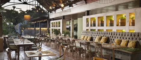 Un restaurante con mesas y sillas de madera, un banco acolchado y lámparas colgantes.