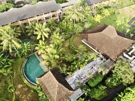 An aerial view of a resort with a swimming pool, palm trees, and a covered patio area.